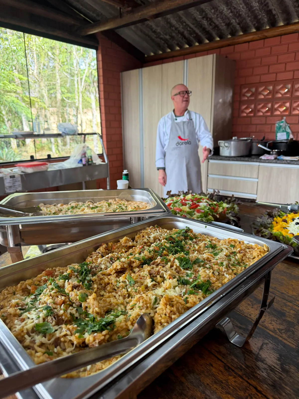 Chef Darela com cubas de arroz e saladas em área de festas